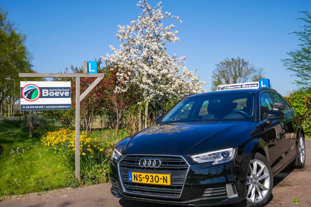 Het bord van Autorijschool Boeve langs de weg met de zwarte lesauto ernaast