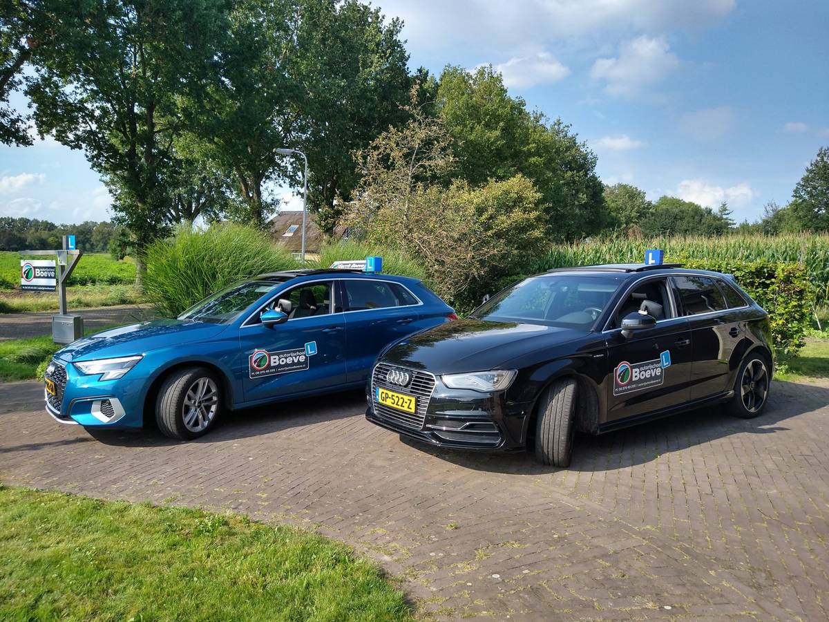 De twee lesauto's van Autorijschool Boeve, een blauwe en een zwarte Audi A3 Sportback met daklicht, aan de weg bij Sint Jansklooster